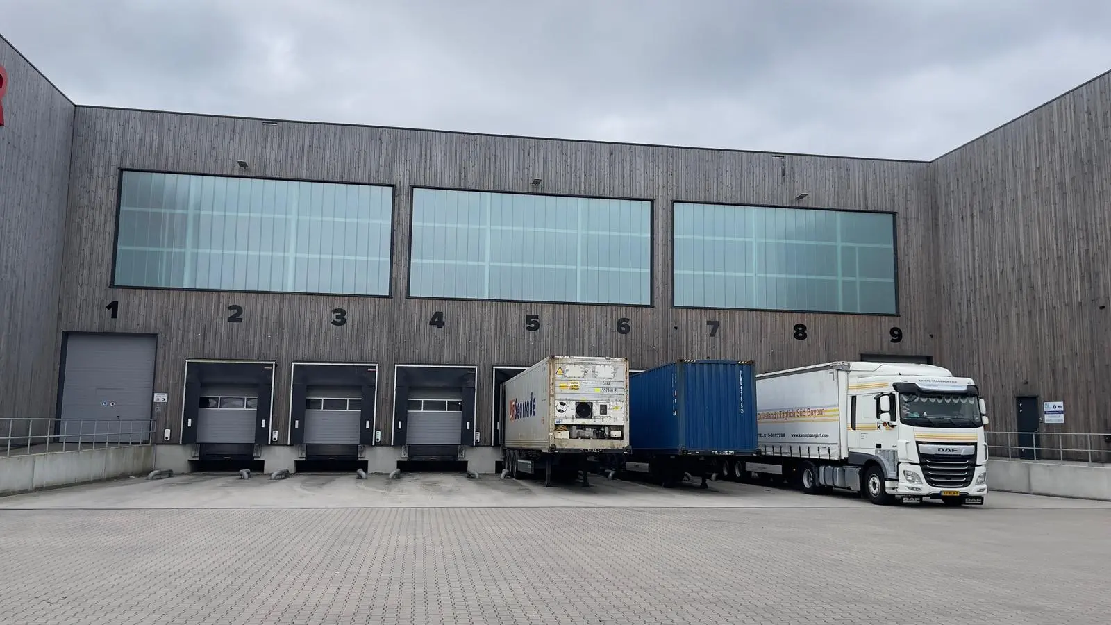 The Reibel warehouse in Hoofddorp: timber-clad hall with loading docks 1 to 9, trucks and containers at the doors